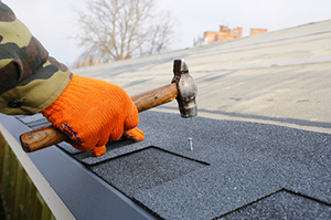 an Ashburn, VA roof repair contractor hammering new shingles into a roof