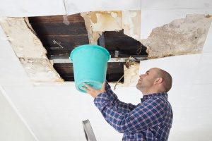 man holding a bucket up to a roof leak that will be repaired by a roof leak repair contractor