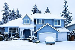 Two story blue house with roof, car in driveway & garden covered in snow