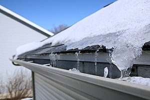 a gutter with icicles on the roof of a home that needs to be fixed by roof repair contractors since the snow caused damaged to it