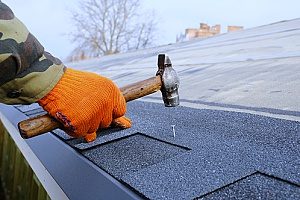 a man hammering new roof shingles onto the top of a house as a part of a Northern Virginia roof repair project