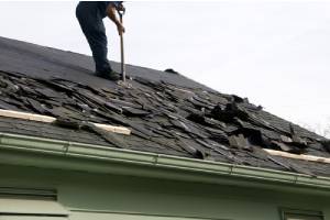 A man removing roof shingles for a new roof installation