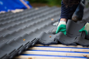 a roofing contractor laying a shingle on a roof being repaired after a storm