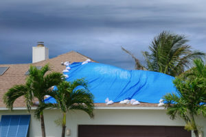 a storm damaged roof with protective blue tarp over holes to prevent further damage