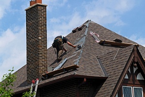 An older home with a damaged roof. A technician is on the roof, inspecting the damage.