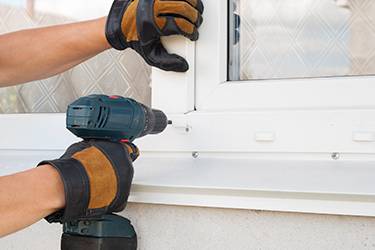 Person with electric screwdriver putting a nail into a window pane